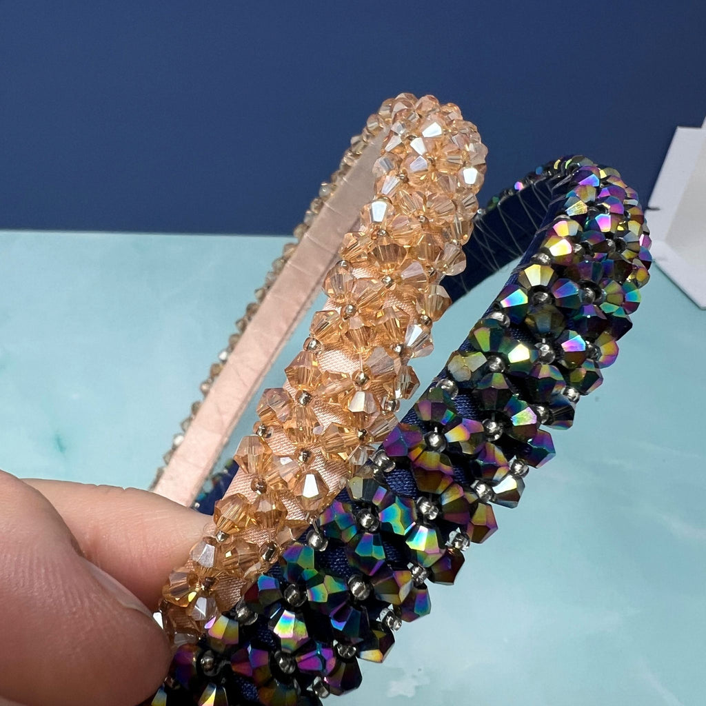Two beaded headbands, one gold and one multicolor, held against a blue background.