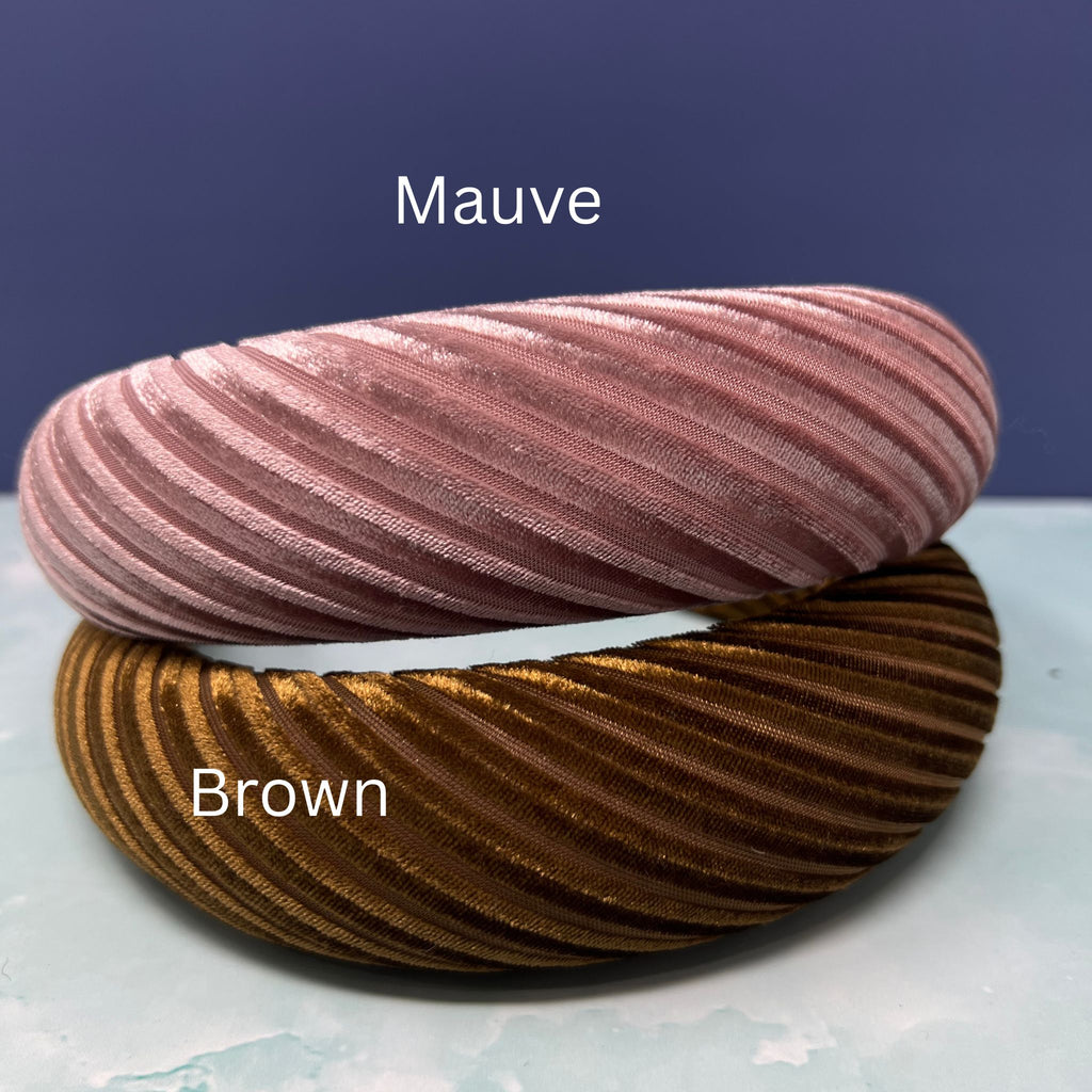 Assorted pleated velvet padded headbands in navy, mauve, light pink, brown, cream, and burgundy stacked in a colorful display.