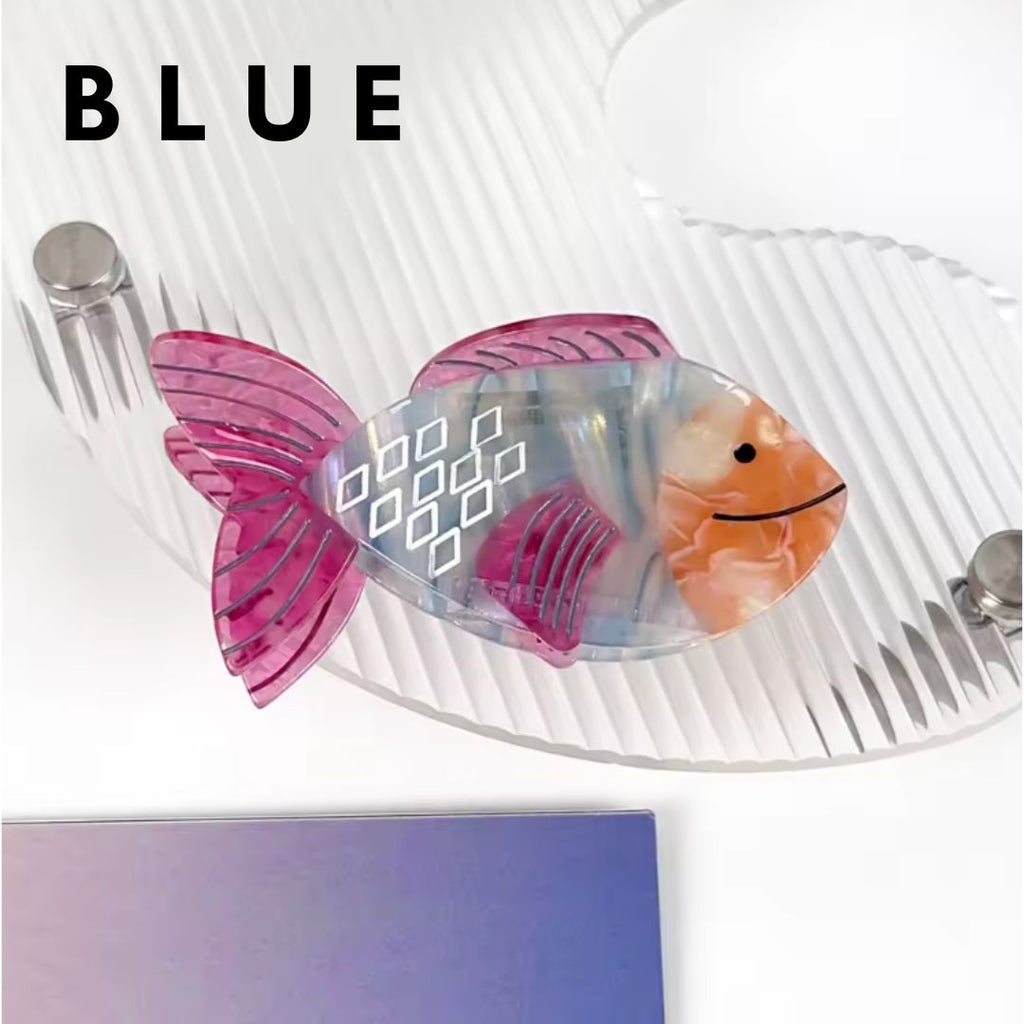 Three colorful fish-shaped hair claw clips in iridescent pink, green, and multicolor designs displayed on a clear wavy tray.