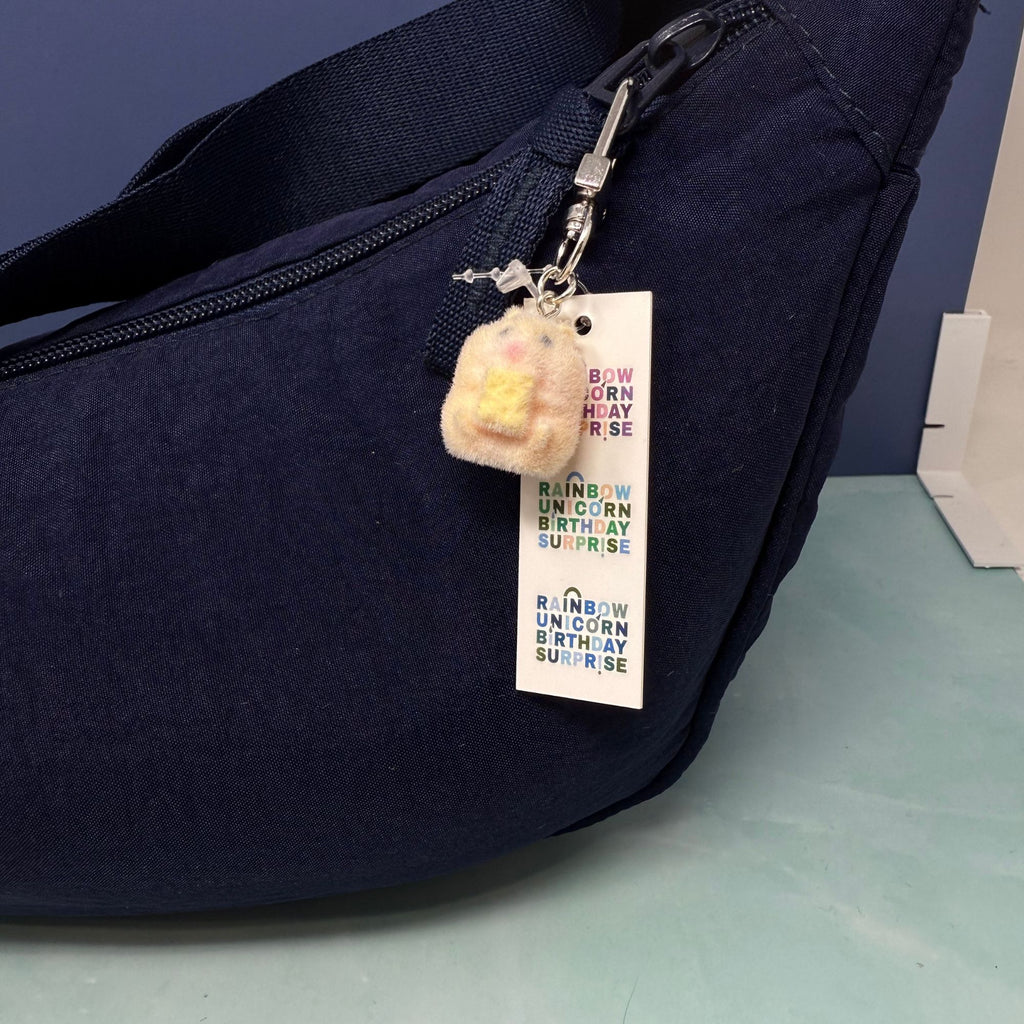 Small fuzzy plush hamster keychain with embroidered face attached to a navy bag.