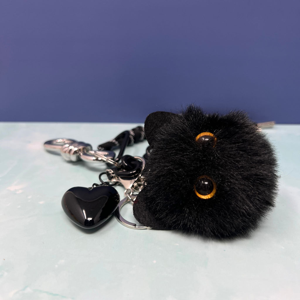 Black cat plush charm keychain with silver chain cluster, black heart, and spike pendant clipped onto hand.