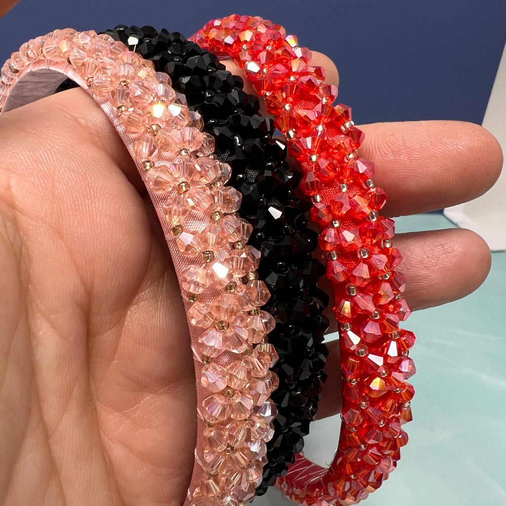 Three beaded hairbands in pink, black, and red held by a hand against a blue background.