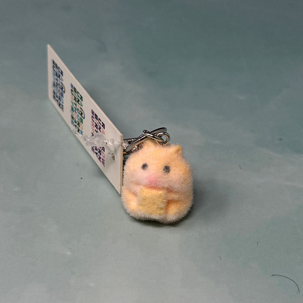 Small fuzzy plush hamster keychain with embroidered face attached to a navy bag.