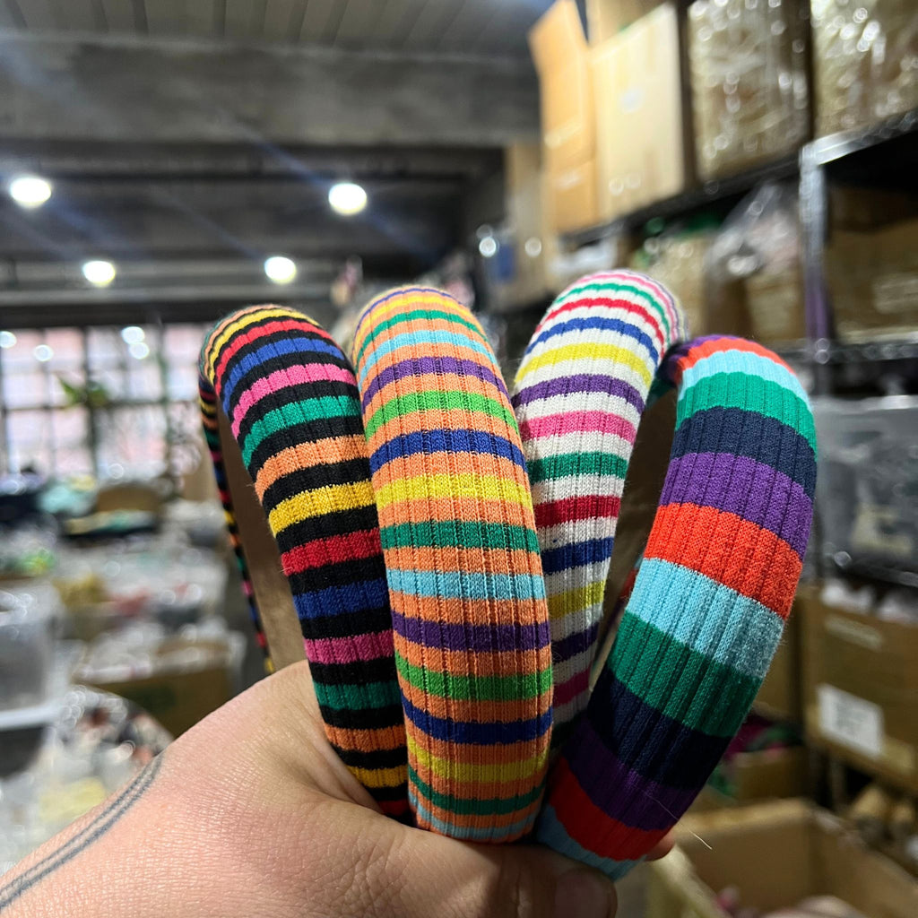 Stack of thick rainbow-striped knit headbands in assorted bold color palettes with one arched to show interior faux suede lining.