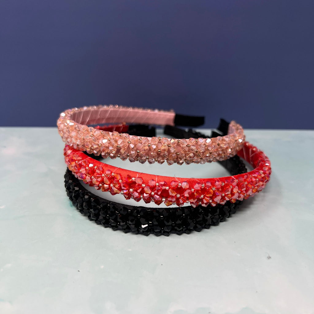 Three rhinestone headbands in black, red, and pink on a white surface with a dark blue background.