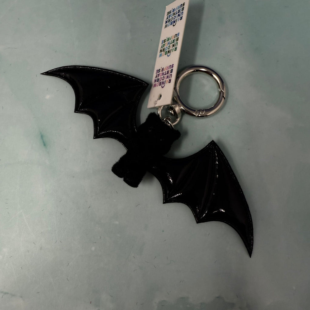 White bat plush keychain hanging from navy bag with large white wings