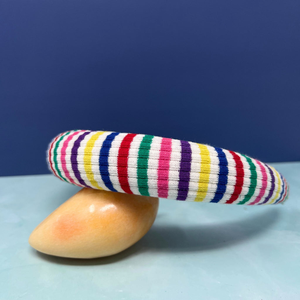 Stack of thick rainbow-striped knit headbands in assorted bold color palettes with one arched to show interior faux suede lining.