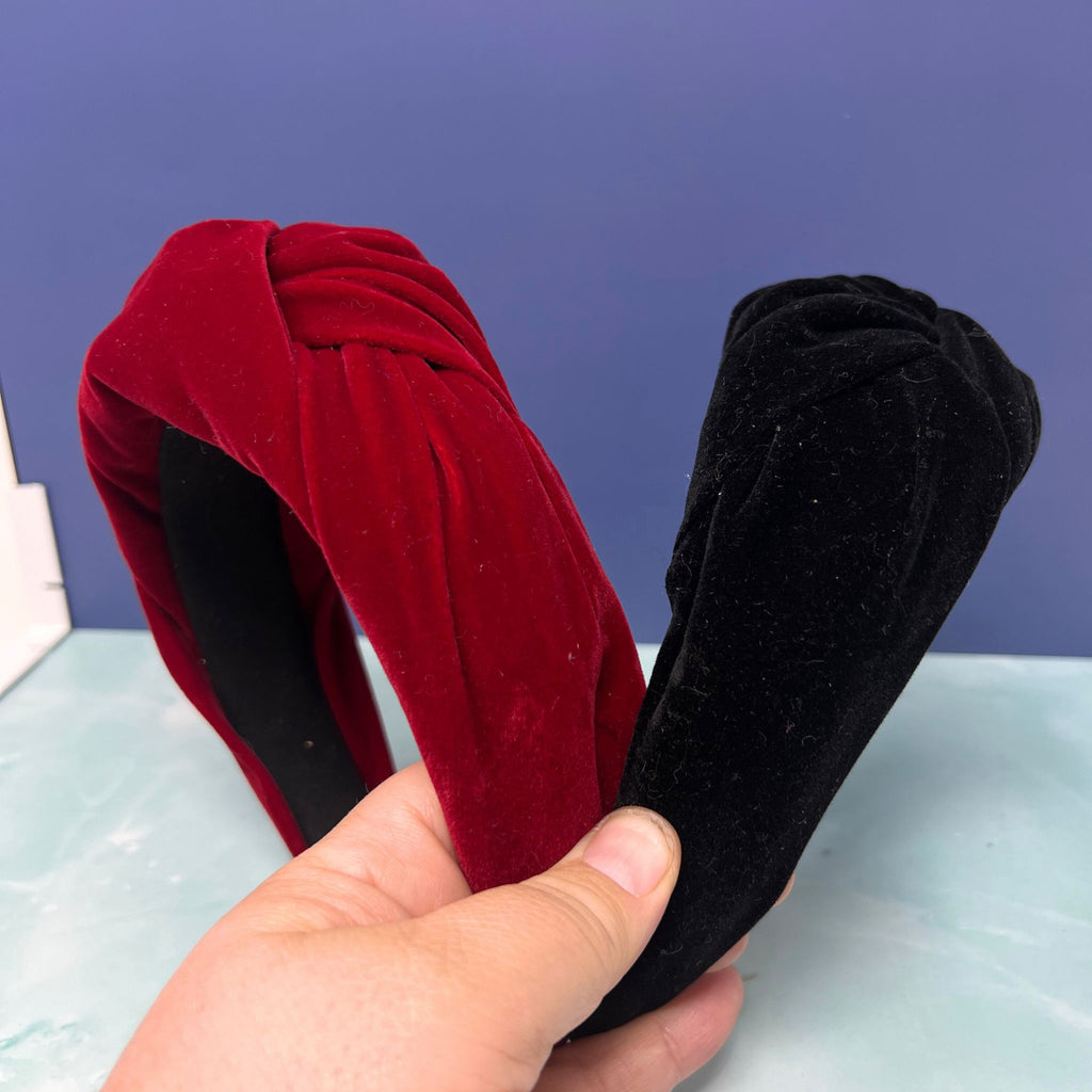 Black and red velvet twist knot headbands stacked together on a light blue surface with a purple background.

