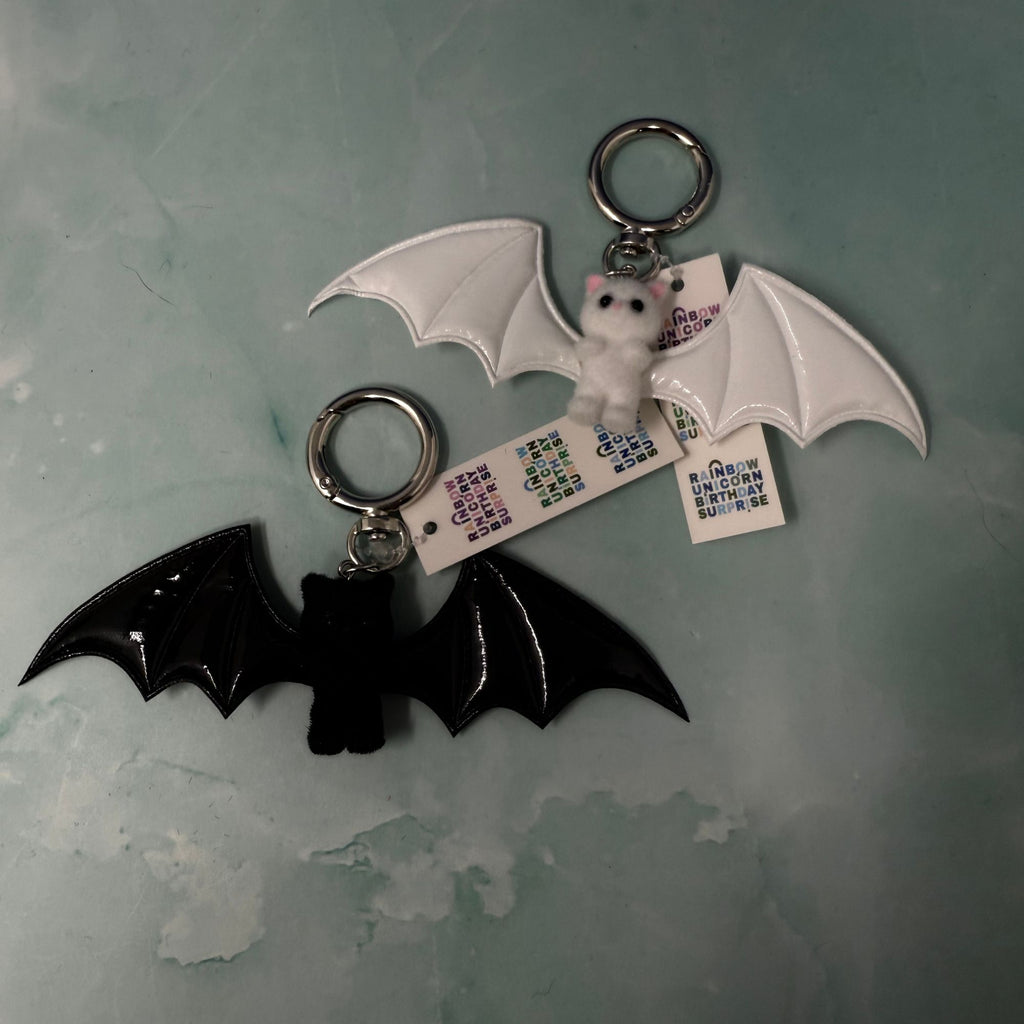 White bat plush keychain hanging from navy bag with large white wings