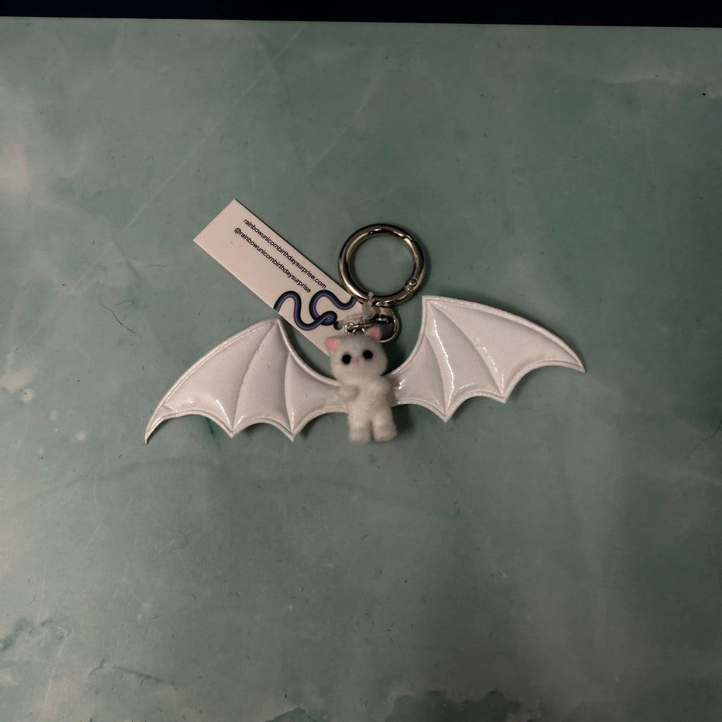 White bat plush keychain hanging from navy bag with large white wings