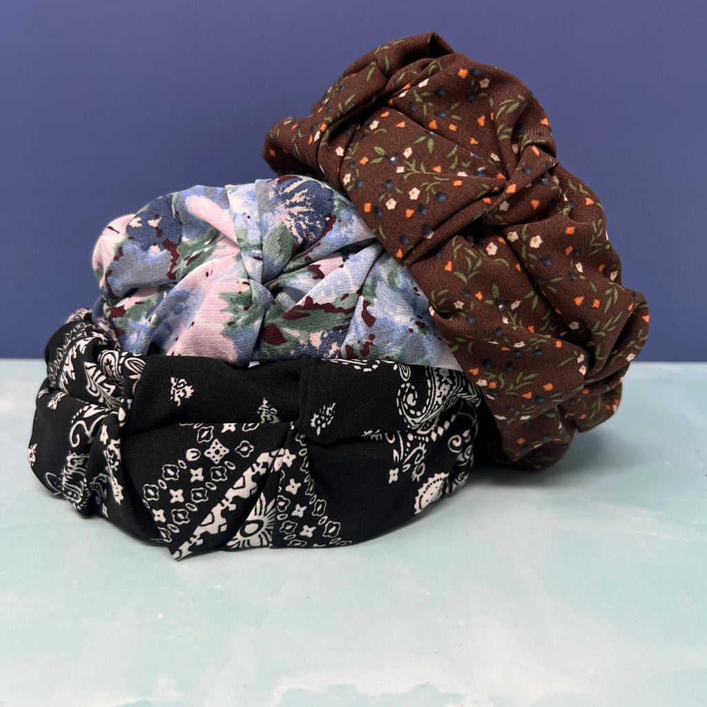 Stack of three knotted headbands featuring brown floral, pastel watercolor floral, and black paisley bandana prints.