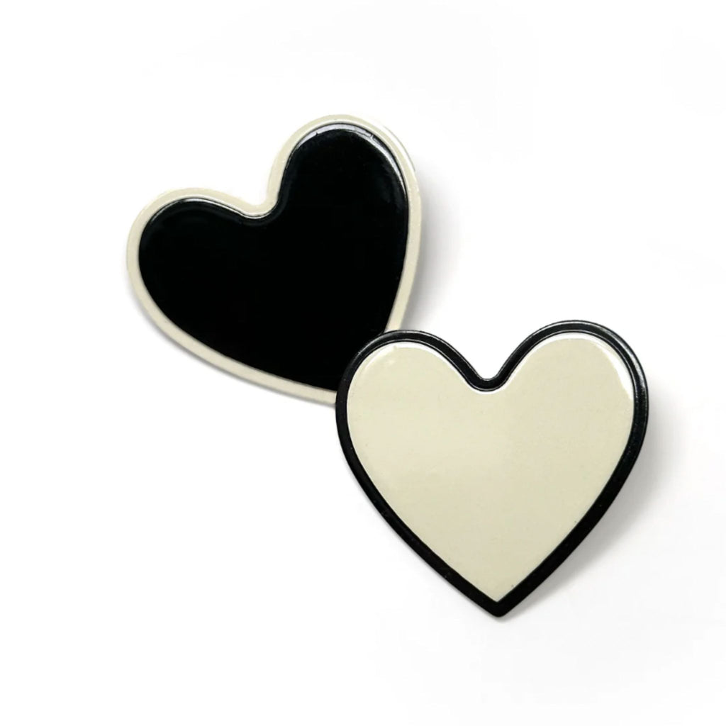 Set of two monochrome heart-shaped hair clips—one black with white outline, one white with black outline—featuring secure alligator clip backing, measuring 1.5 inches wide by 1.75 inches high.