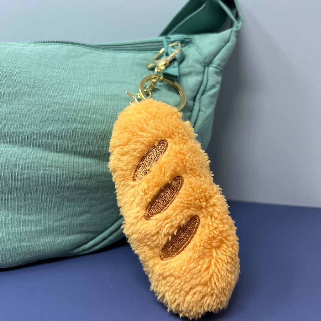 Plush brown bread loaf keychain with embroidered scoring, approx. 4 inches long and 1.5 inches wide