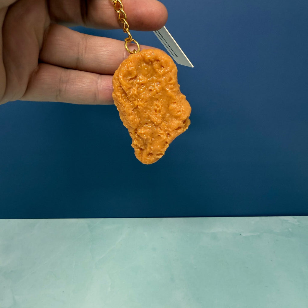 Realistic chicken nugget keychain with gold key ring, hyper-detailed faux nugget accessory used as a funny bag charm.
