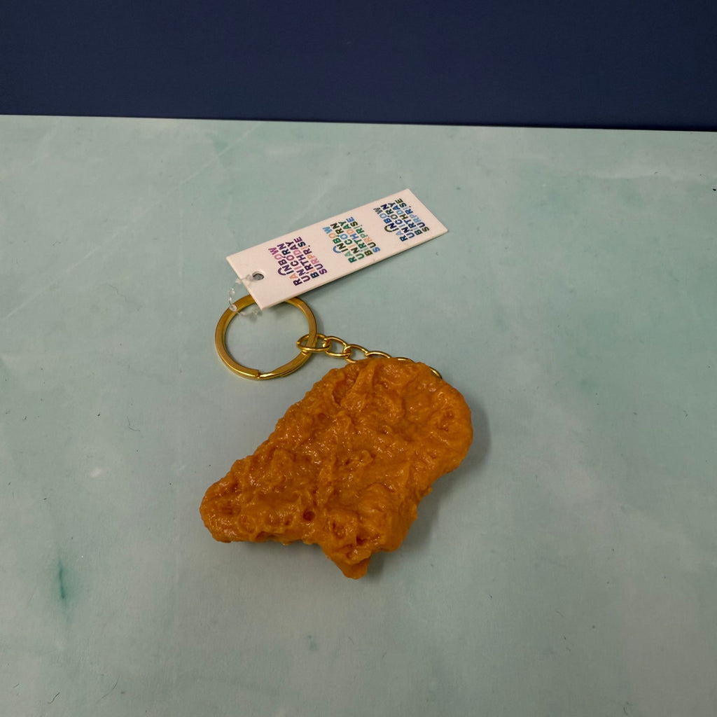 Realistic chicken nugget keychain with gold key ring, hyper-detailed faux nugget accessory used as a funny bag charm.