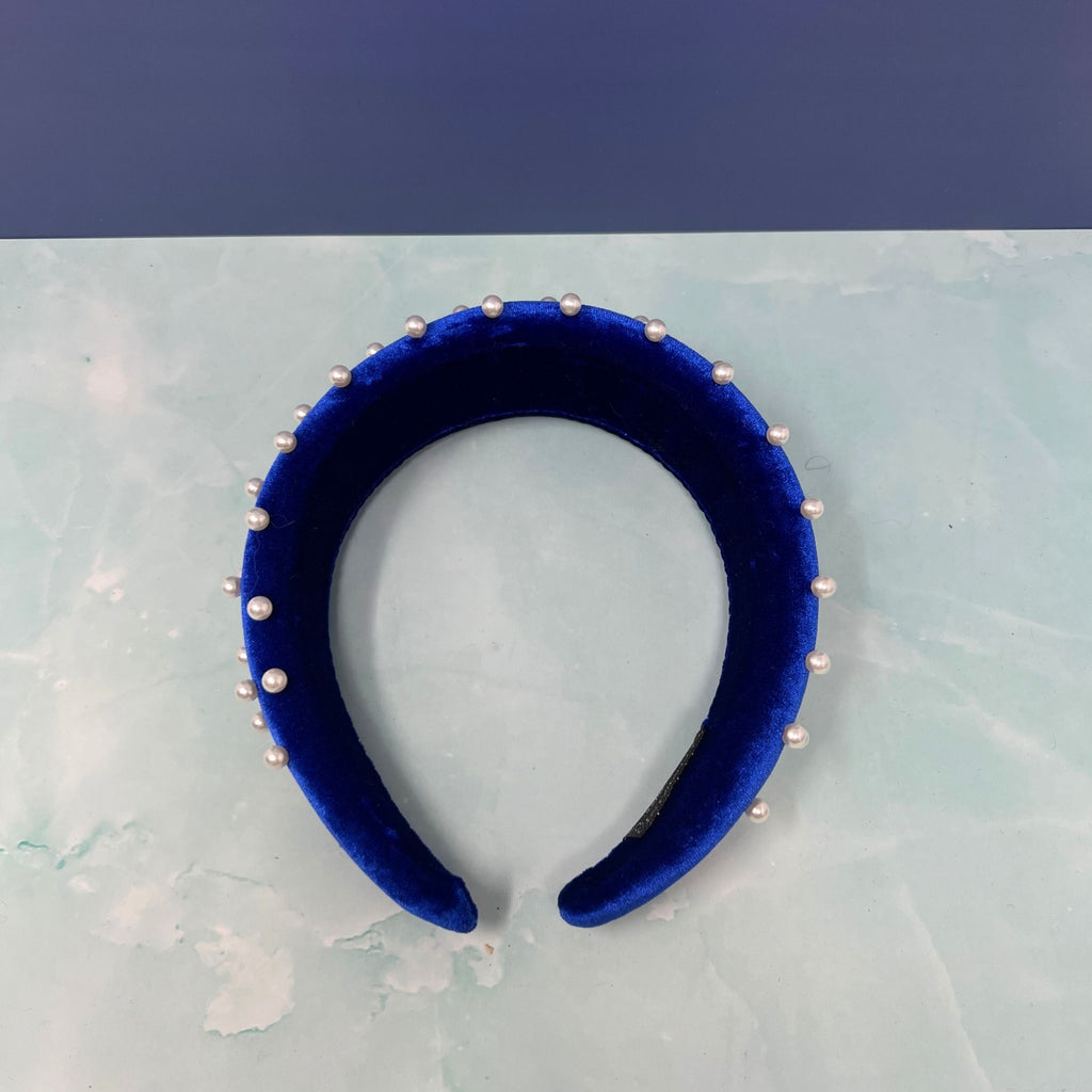Stacked velvet headbands in pink, black, ivory, and royal blue, each embellished with faux pearls for a chic and elegant look.