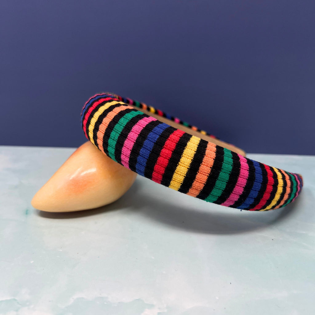 Stack of thick rainbow-striped knit headbands in assorted bold color palettes with one arched to show interior faux suede lining.