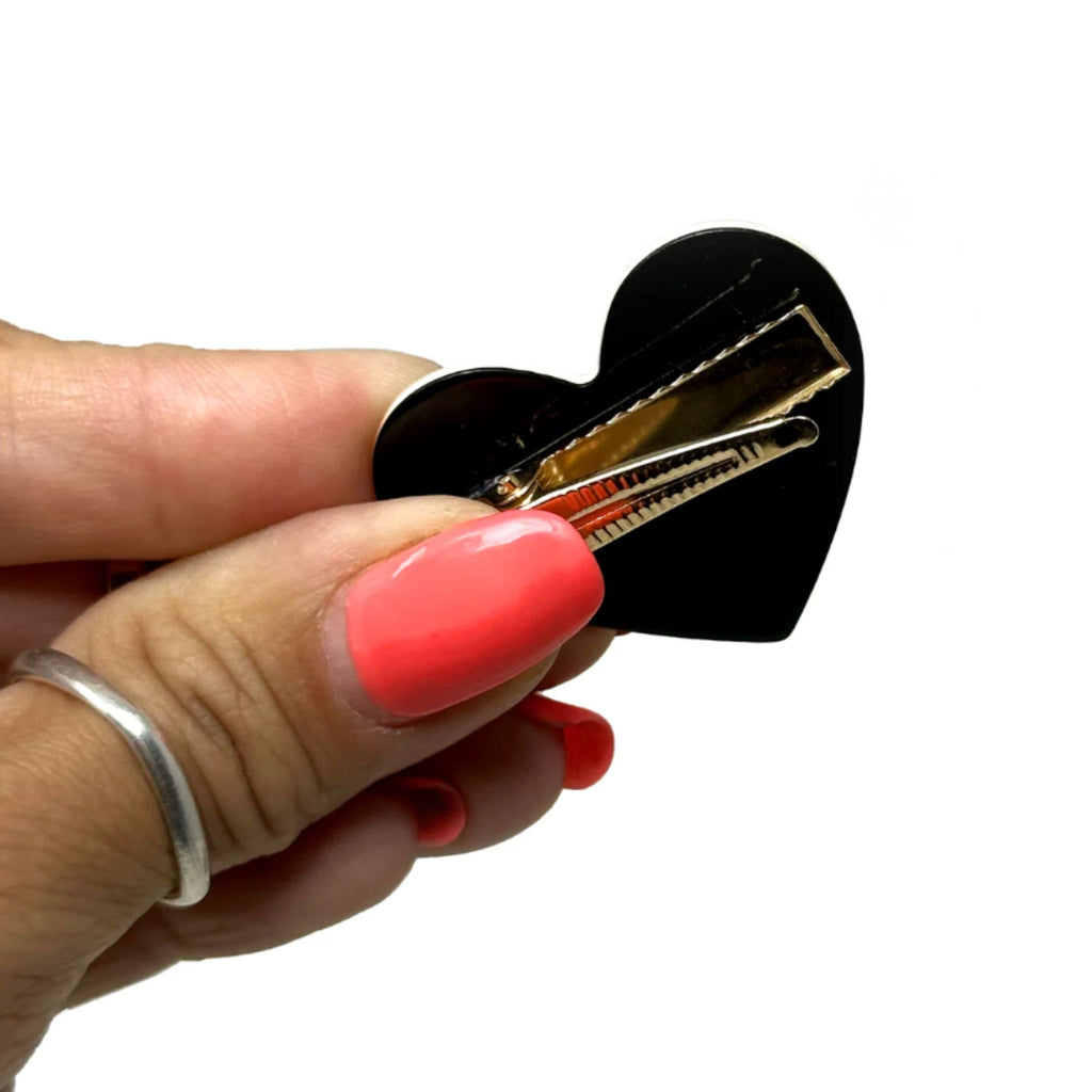 Set of two monochrome heart-shaped hair clips—one black with white outline, one white with black outline—featuring secure alligator clip backing, measuring 1.5 inches wide by 1.75 inches high.