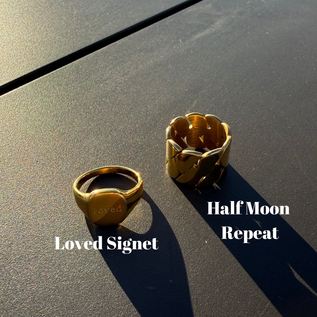 Two gold rings labeled 'Loved Signet' and 'Half Moon Repeat' on a textured surface.