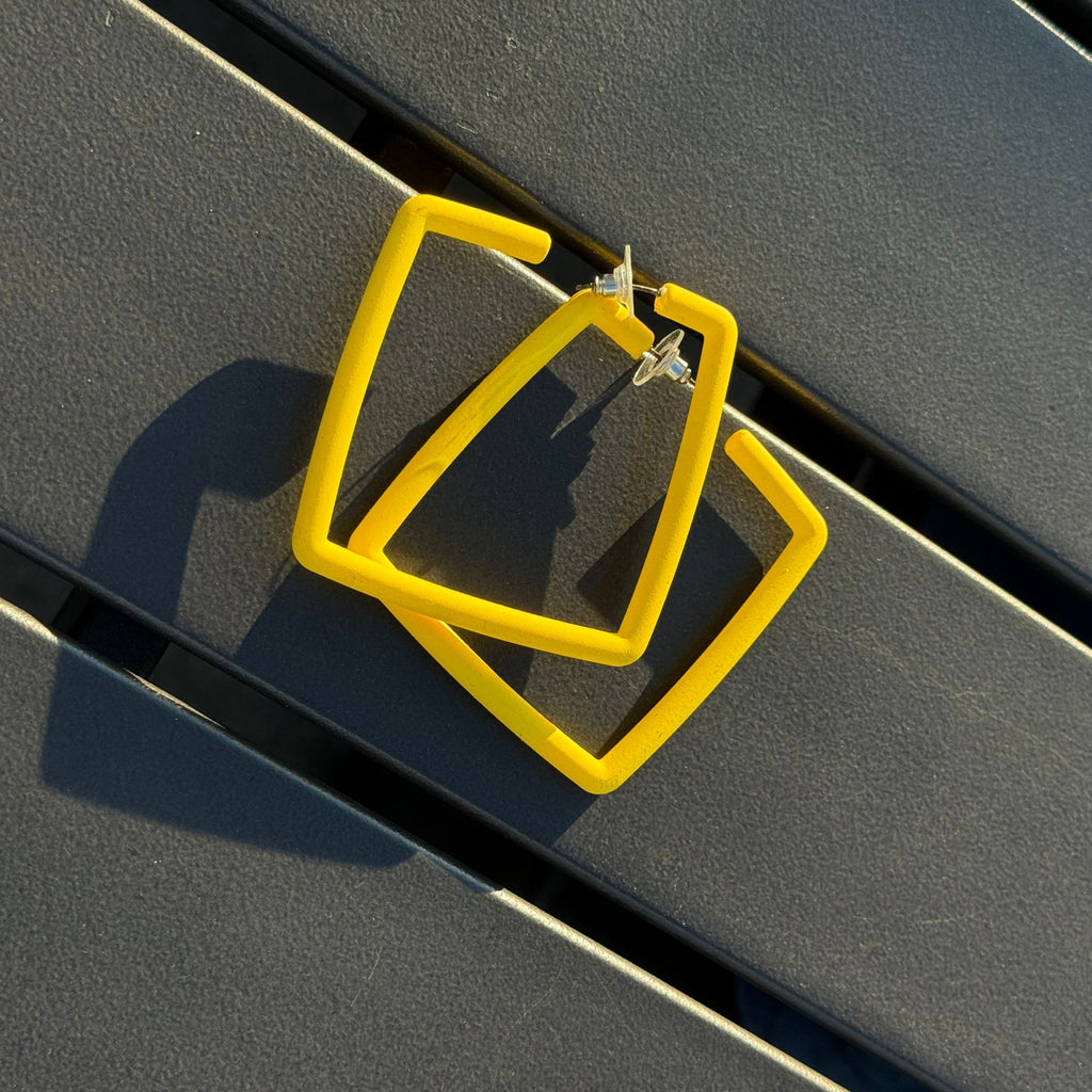 Yellow square hoop earrings on a dark surface