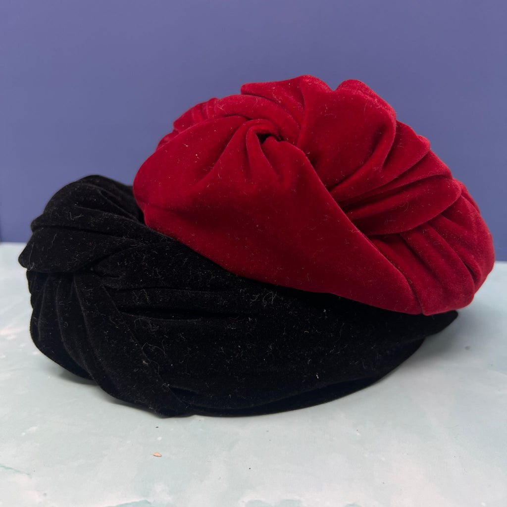 Black and red velvet twist knot headbands stacked together on a light blue surface with a purple background.

