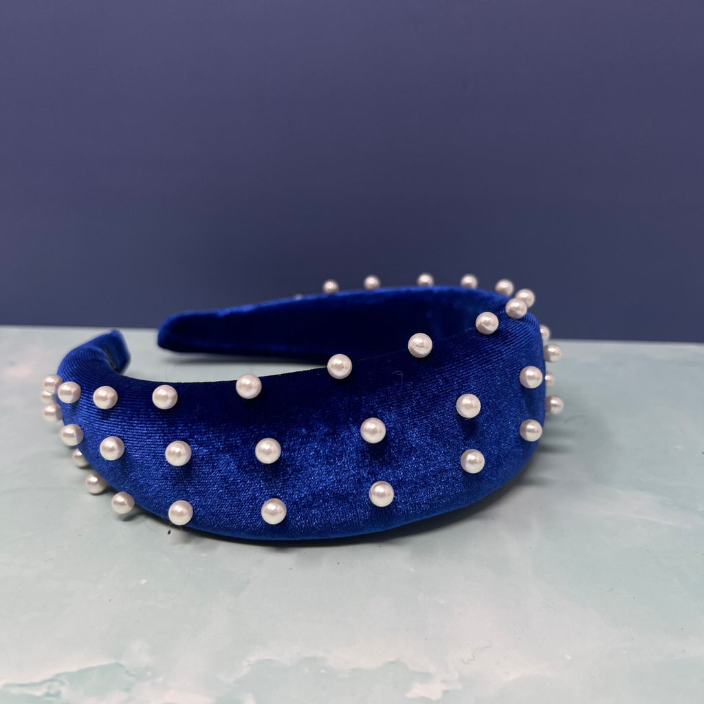 Stacked velvet headbands in pink, black, ivory, and royal blue, each embellished with faux pearls for a chic and elegant look.