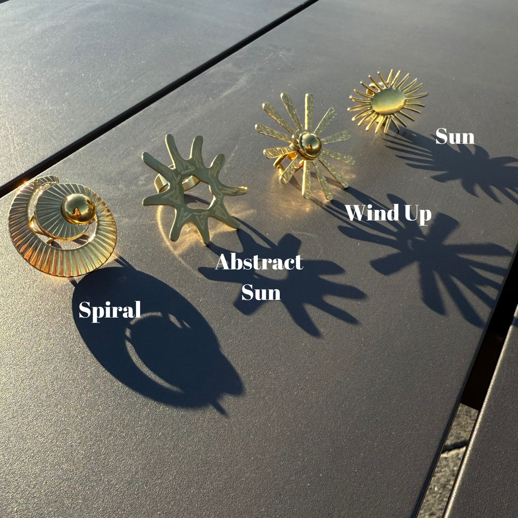 Gold sun-shaped earrings on a dark surface with labels indicating design names.