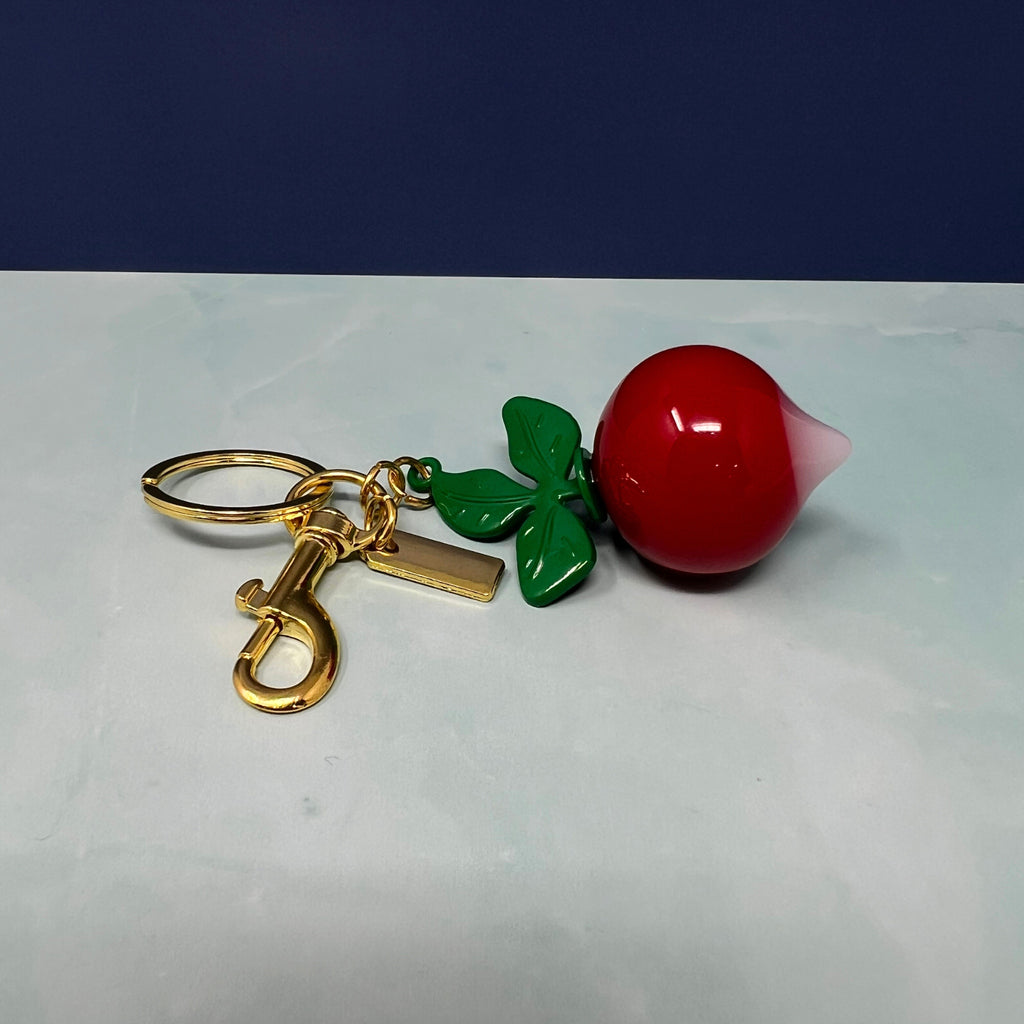 Radish keychain with glossy red root, white tip, green enamel leaves, and gold hardware displayed against a light background