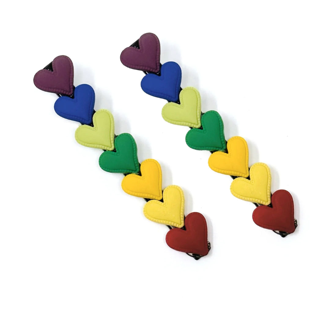 Set of two rainbow heart barrettes measuring approximately 3.5"W x 0.5"H, featuring vibrant multi-color designs with secure clip backing.