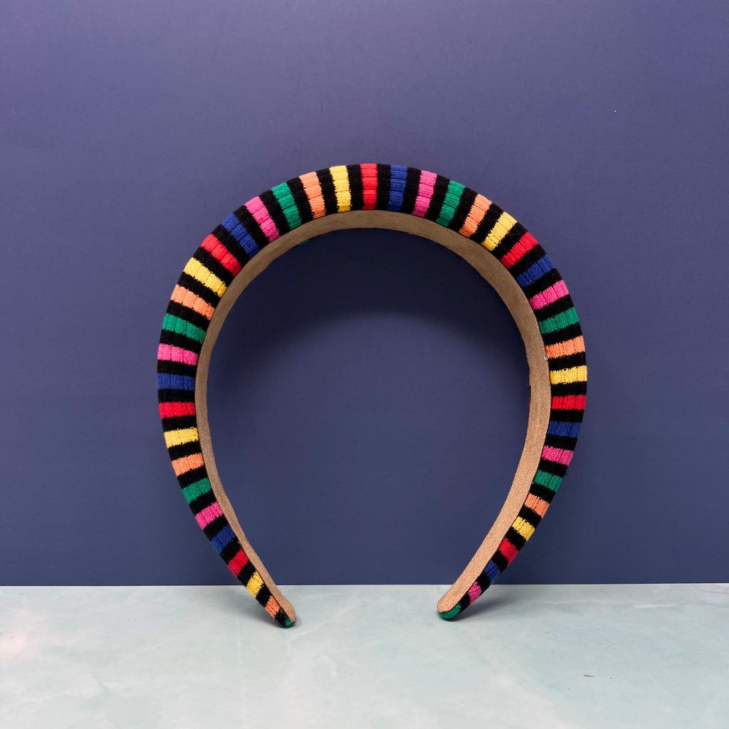Stack of thick rainbow-striped knit headbands in assorted bold color palettes with one arched to show interior faux suede lining.