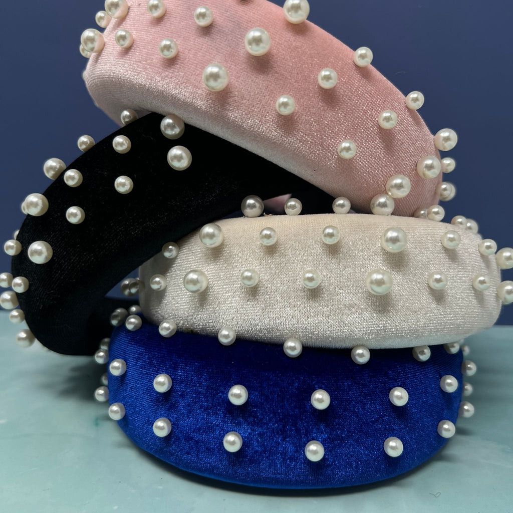 Stacked velvet headbands in pink, black, ivory, and royal blue, each embellished with faux pearls for a chic and elegant look.