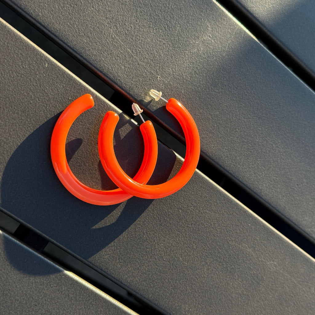 Orange hoop earrings on a reflective black surface