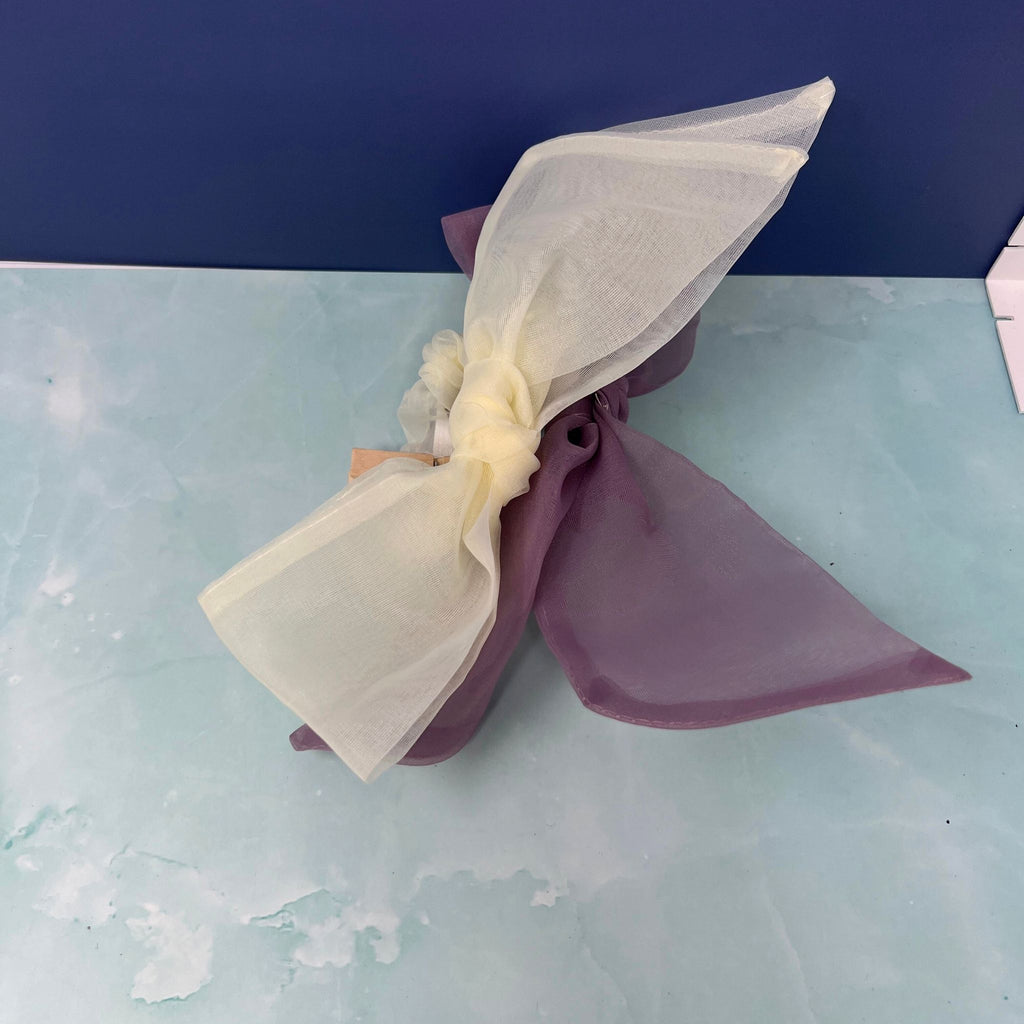 Sheer organza bow scrunchie in cream and lavender with oversized flowing tails, styled on a pastel background.

