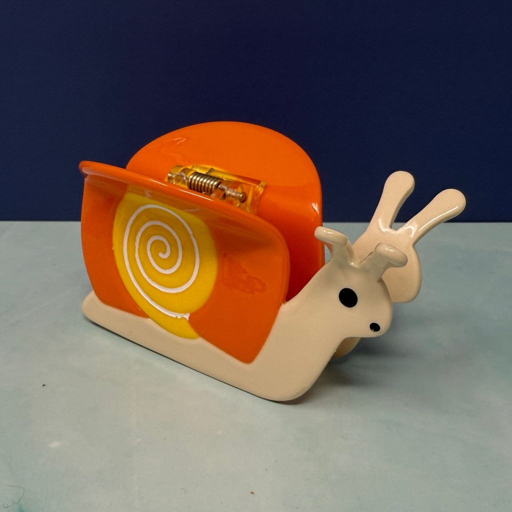 Orange snail hair claw clip with yellow swirl shell, glossy acetate finish, and secure spring grip