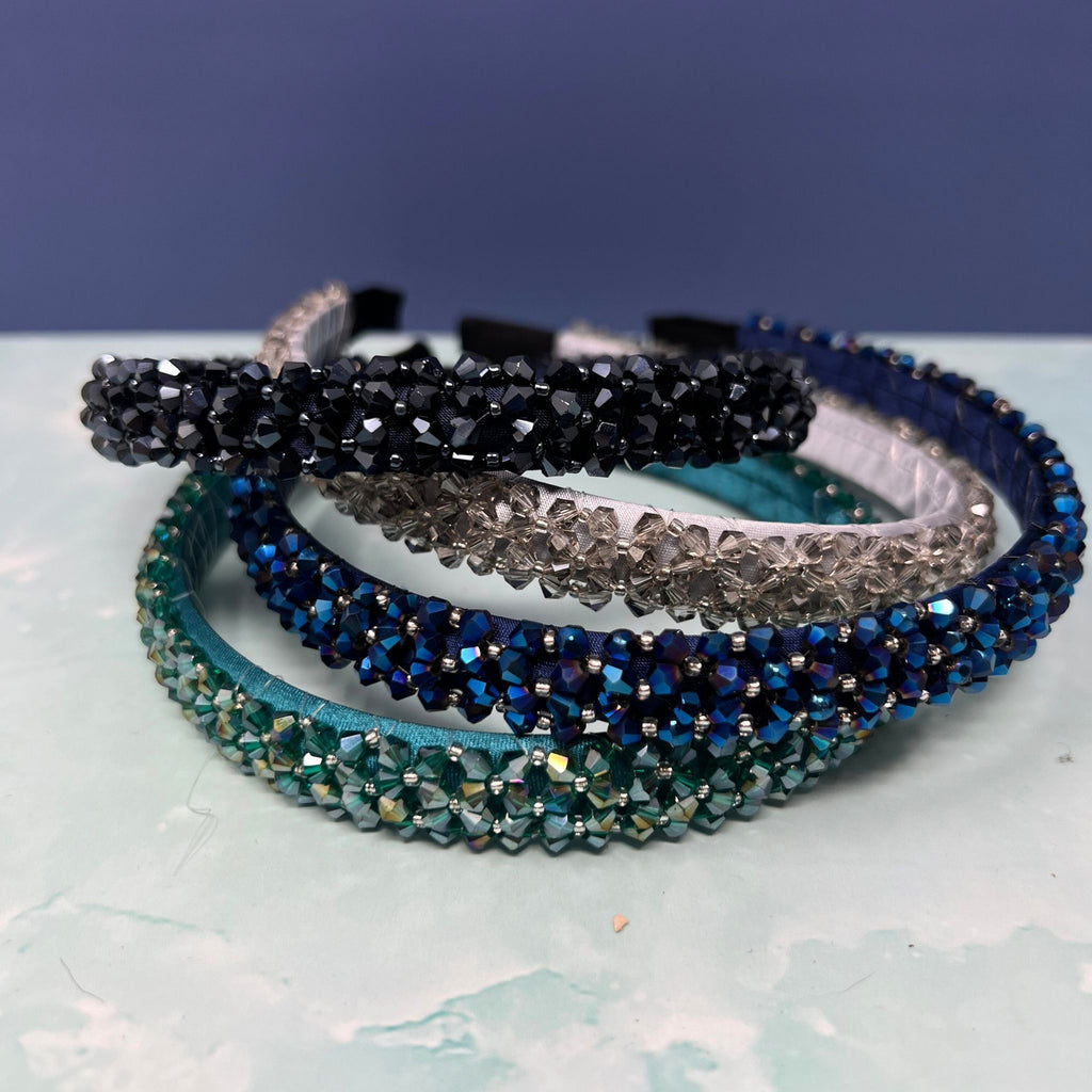 Three crystal beaded skinny headbands in pink, red, and black stacked on a light surface against a navy background.