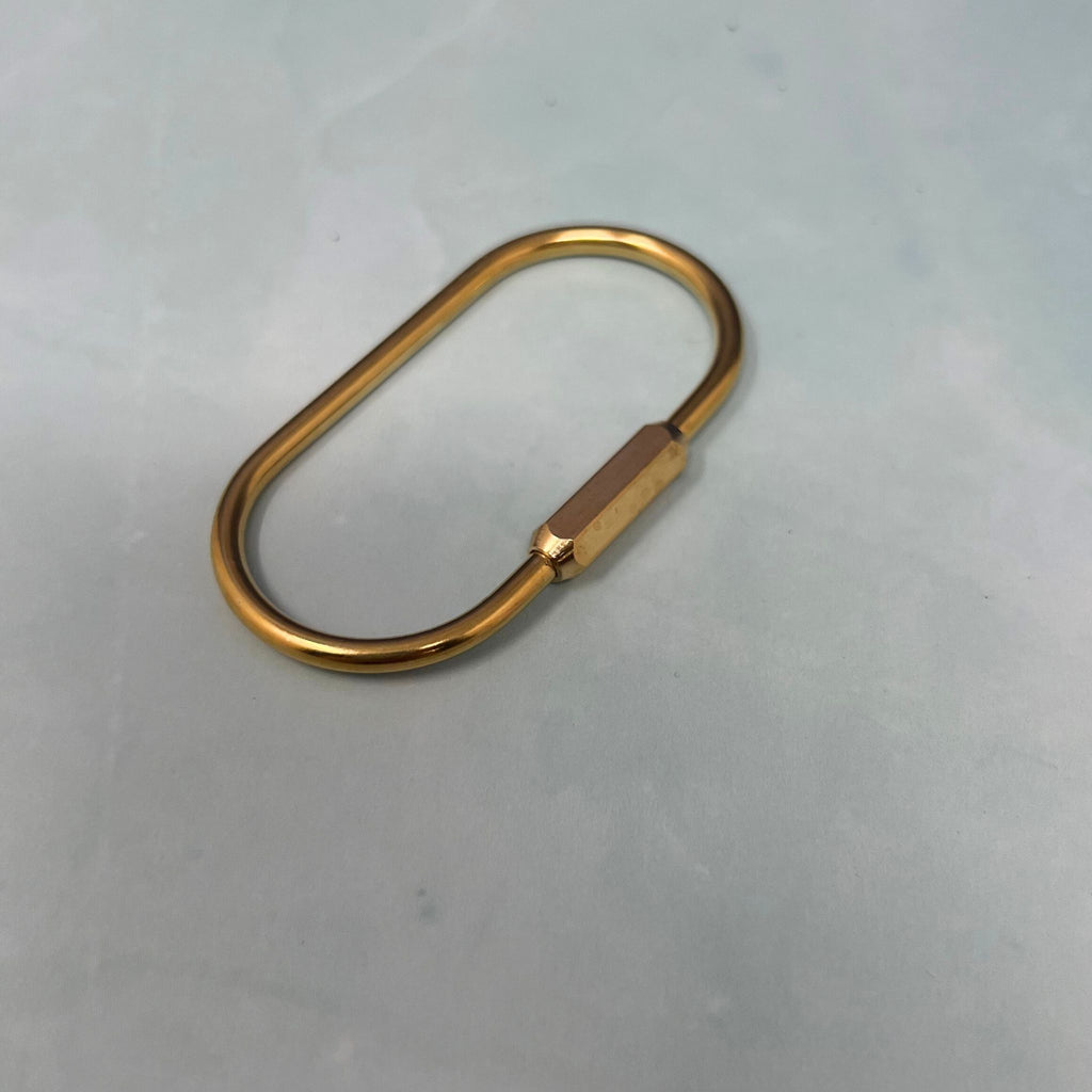 Flat lay of assorted geometric brass key rings including teardrop, oval, rectangle, half-moon, and paperclip shapes on a light blue surface.