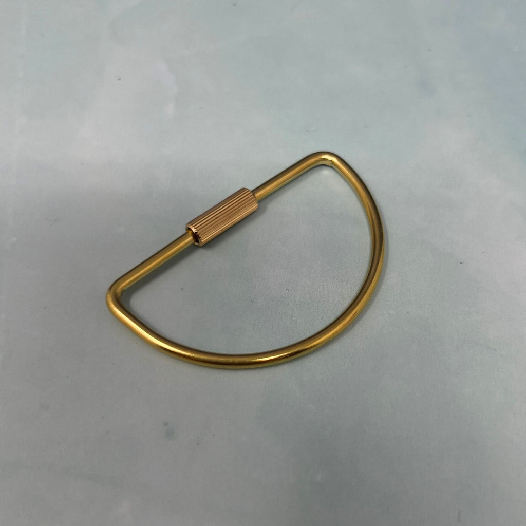 Flat lay of assorted geometric brass key rings including teardrop, oval, rectangle, half-moon, and paperclip shapes on a light blue surface.