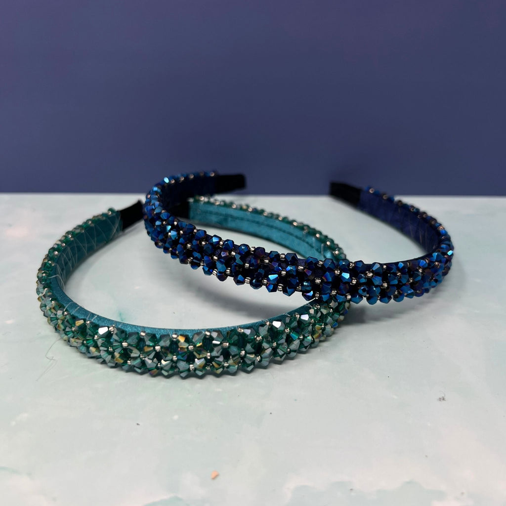 Two blue beaded headbands on a light surface with a dark background