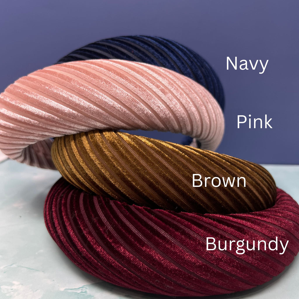 Assorted pleated velvet padded headbands in navy, mauve, light pink, brown, cream, and burgundy stacked in a colorful display.