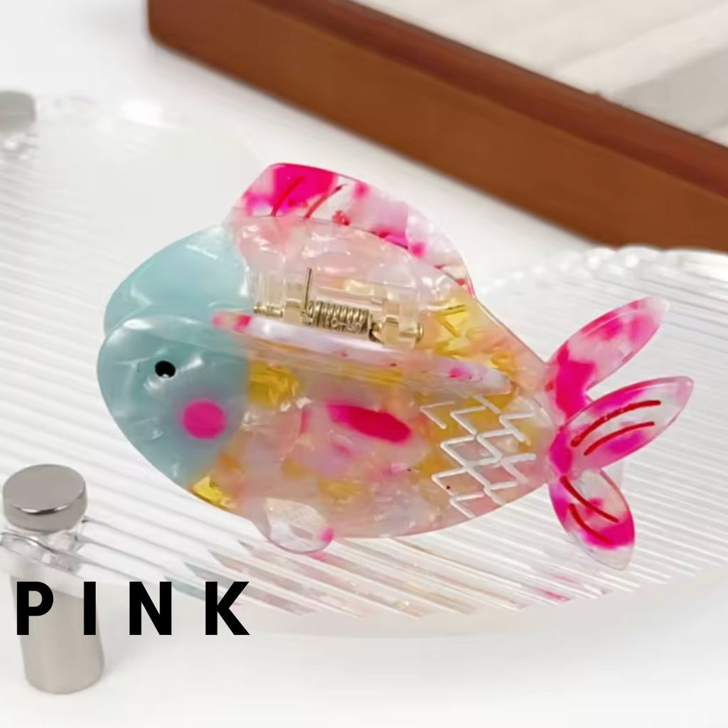 Three colorful fish-shaped hair claw clips in iridescent pink, green, and multicolor designs displayed on a clear wavy tray.