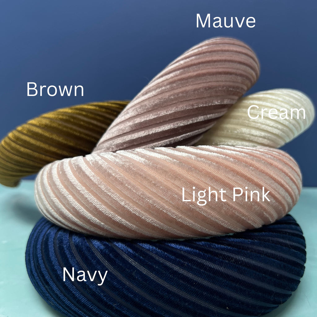 Assorted pleated velvet padded headbands in navy, mauve, light pink, brown, cream, and burgundy stacked in a colorful display.