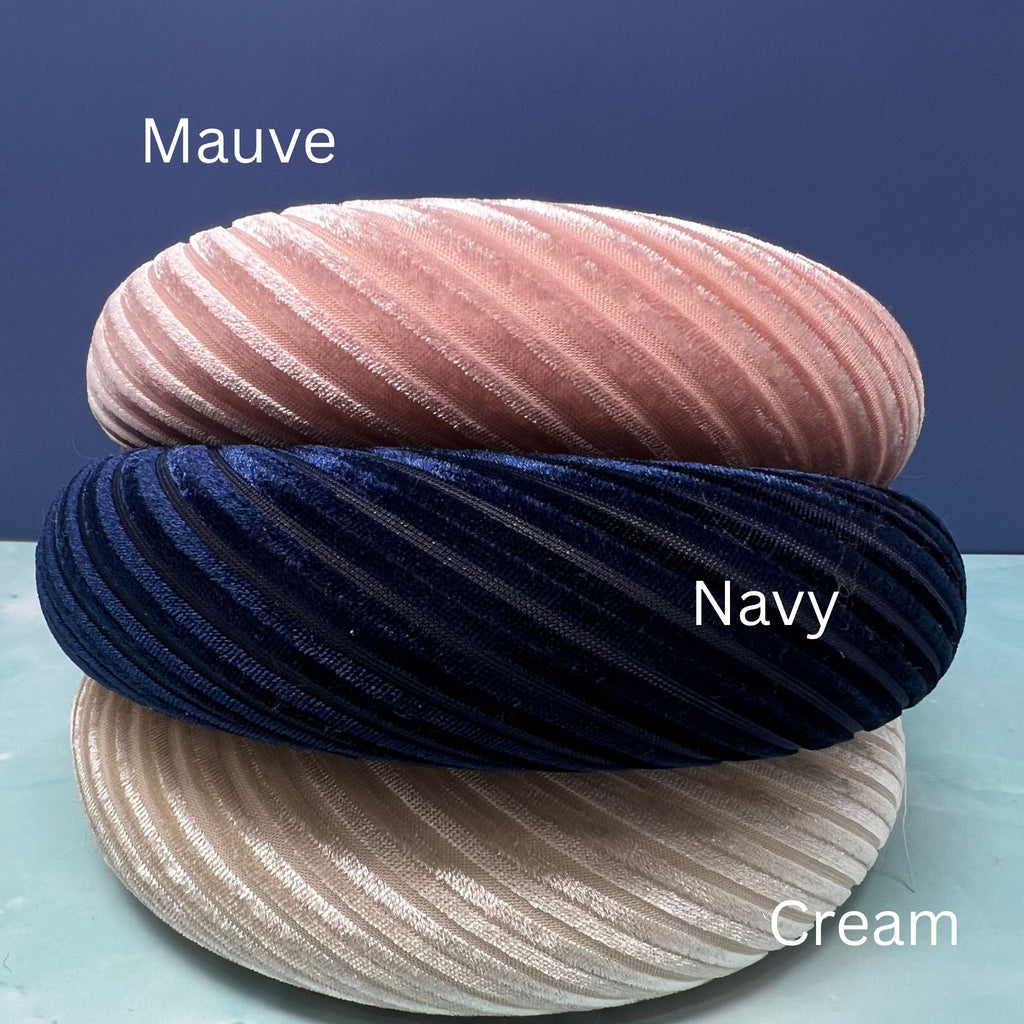 Assorted pleated velvet padded headbands in navy, mauve, light pink, brown, cream, and burgundy stacked in a colorful display.