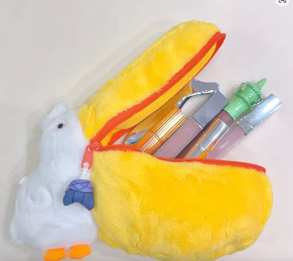 Plush pelican makeup bag with a yellow zippered beak open, holding lip glosses and beauty items, with a fluffy white head and orange feet.