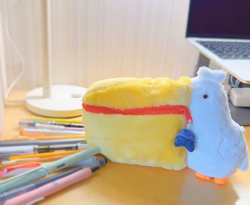 Plush pelican makeup bag with a yellow zippered beak open, holding lip glosses and beauty items, with a fluffy white head and orange feet.
