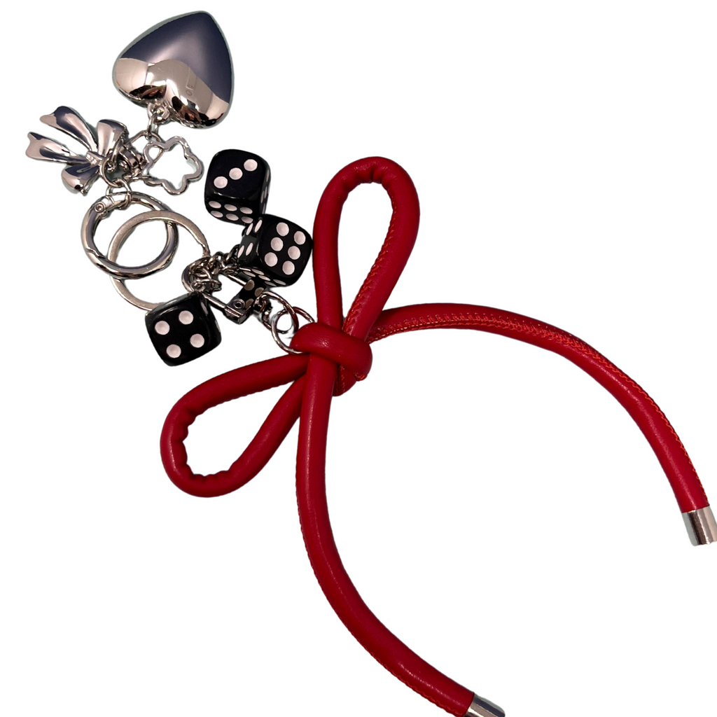 Red faux leather bow keychain with black dice charms, silver heart, and flower detail on a white background