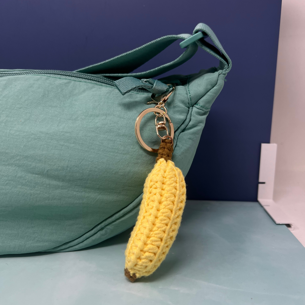 Crochet banana keychain with gold keyring and clasp hanging on a light teal bag.