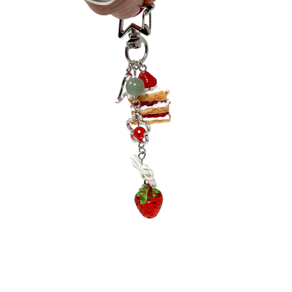 Mini strawberry shortcake keychain with dangling cake slice and strawberry charm on star-shaped clasp.